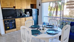 Uma cozinha com armários de madeira, fogão preto e geladeira azul. Há uma mesa de jantar com cadeiras brancas e pratos azuis.