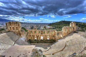 Ein uraltes Amphitheater mit Steinsitzen und Ruinen, umgeben von einer Stadtlandschaft und Hügeln.