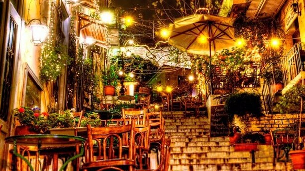 Ein Straßencafé mit Tischen, Stühlen, einer Treppe und Topfpflanzen.