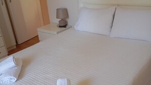Ein ordentlich bezogenes Bett mit weißen Leinen und Handtüchern, eine Nachttischlampe und ein weißer Nachttisch.