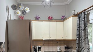 A compact kitchen with a dining area, featuring a refrigerator, stove, sink, and a chandelier. - Cozy Apartment in the Heart of Athens (Zografos)