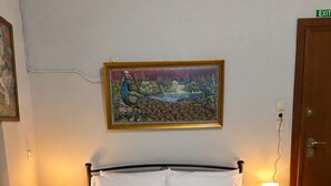 A neatly made bed with white linens and two folded towels, a painting of a peacock above the bed, and two bedside lamps on nightstands. - Cozy Apartment in the Heart of Athens (Zografos)