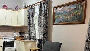 A compact living space with a sofa bed, a kitchen area with a stove and sink, and a painting on the wall. - Cozy Apartment in the Heart of Athens (Zografos)