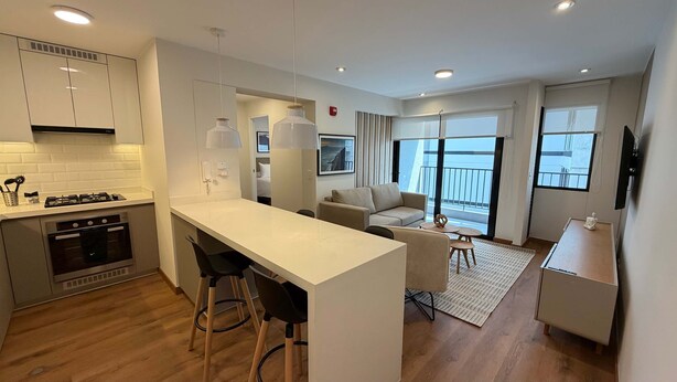 A modern kitchen with a central island, a dining area with a sofa and table, and a balcony with a view. - w Amazing and Cozy 2BR w Balcony in Miraflores (Lima)