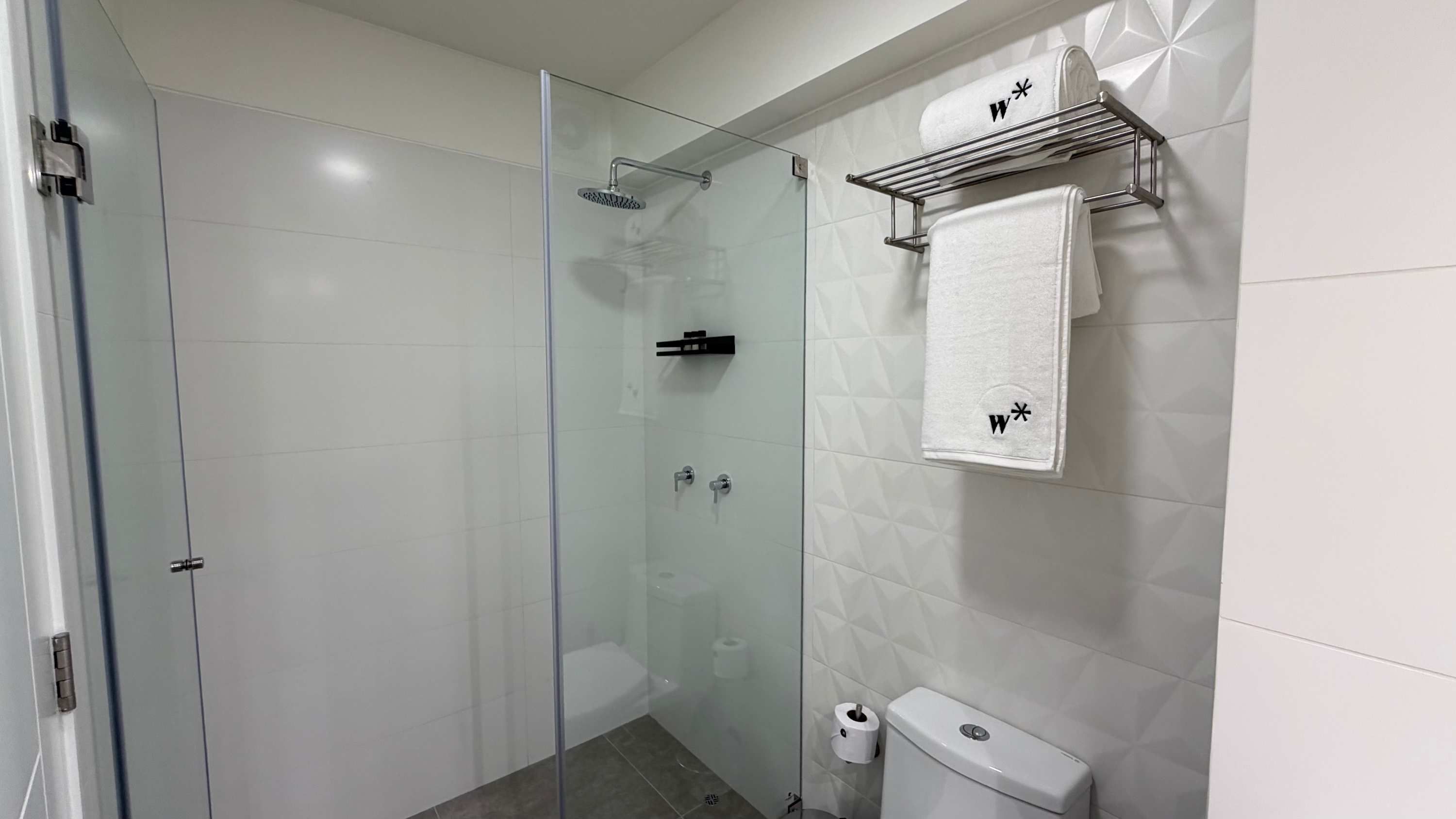 A modern bathroom with a glass-enclosed shower, a toilet, and a towel rack with towels.