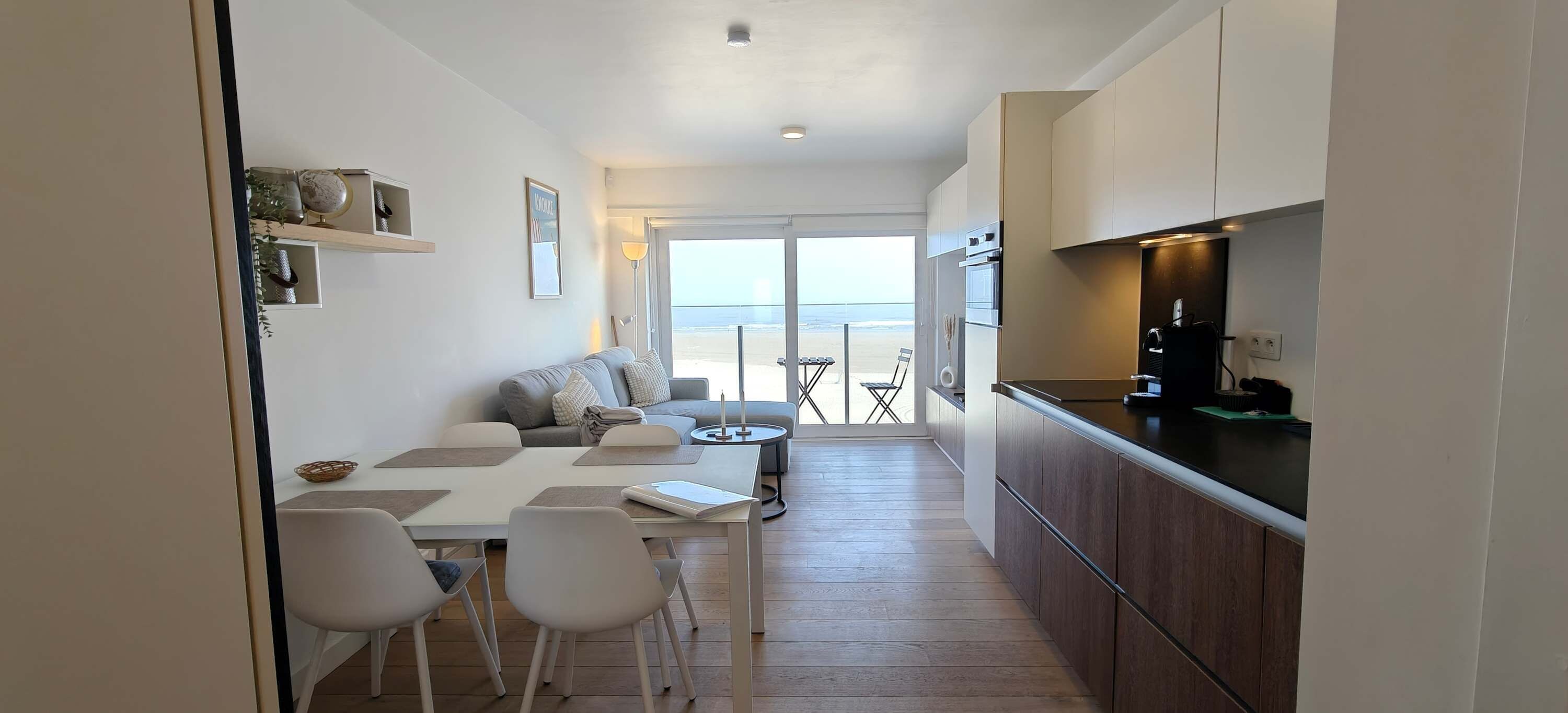 A modern kitchen with a dining area, a sofa, and a view to the sea.
