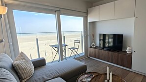 Ein modernes Wohnzimmer mit großem Fernseher, einer Couch und Blick auf den Strand.