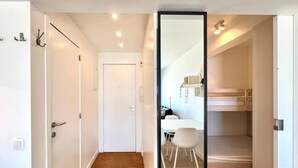 Een moderne, minimalistisch ingerichte kamer met een houten vloer, witte muren, een witte deur en een grote spiegel.