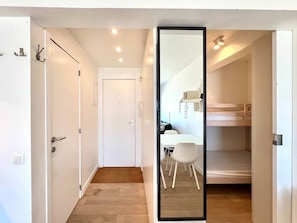 Quarto moderno e minimalista com piso de madeira, paredes brancas e uma porta branca, além de um espelho grande.