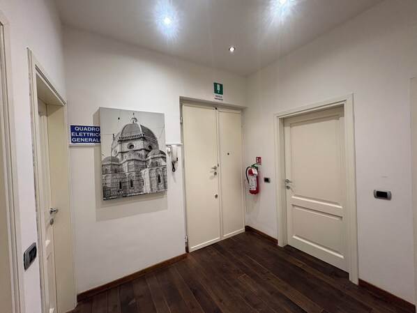 Un couloir avec trois portes blanches, un extincteur et un panneau indiquant la sortie de secours, fixé au mur.