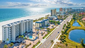 A beachfront hotel with multiple buildings, a swimming pool, and a road with palm trees. - SUMMER SPECIAL RATES!!!  2B/2B NEWLY REMODELED BEACHFRONT CORNER CONDO AT SHAMRON BEACH CLUB 308! POOL! (Fort Myers Beach)