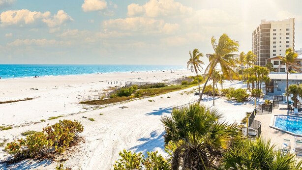 A beach resort with a pool, palm trees, and a view of the ocean. - SUMMER SPECIAL RATES!!!  2B/2B NEWLY REMODELED BEACHFRONT CORNER CONDO AT SHAMRON BEACH CLUB 308! POOL! (Fort Myers Beach)