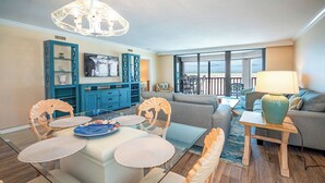 A living room with a glass dining table, blue cabinets, a sofa, and a view of the beach. - SUMMER SPECIAL RATES!!!  2B/2B NEWLY REMODELED BEACHFRONT CORNER CONDO AT SHAMRON BEACH CLUB 308! POOL! (Fort Myers Beach)