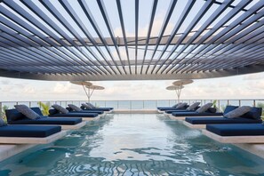 Ein Rooftop-Infinity-Pool mit Liegestühlen und Sonnenschirmen, der einen Blick auf den Ozean bietet.