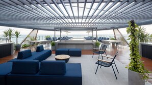 Eine Dachterrasse mit blauen Sitzgelegenheiten, einem Holztisch und Topfpflanzen.