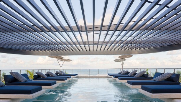 Ein Rooftop-Infinity-Pool mit Liegestühlen und Sonnenschirmen, der einen Blick auf den Ozean bietet.