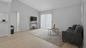 En moderne stue med en grå sofa, et rundt sofabord og et fjernsyn på et stativ.