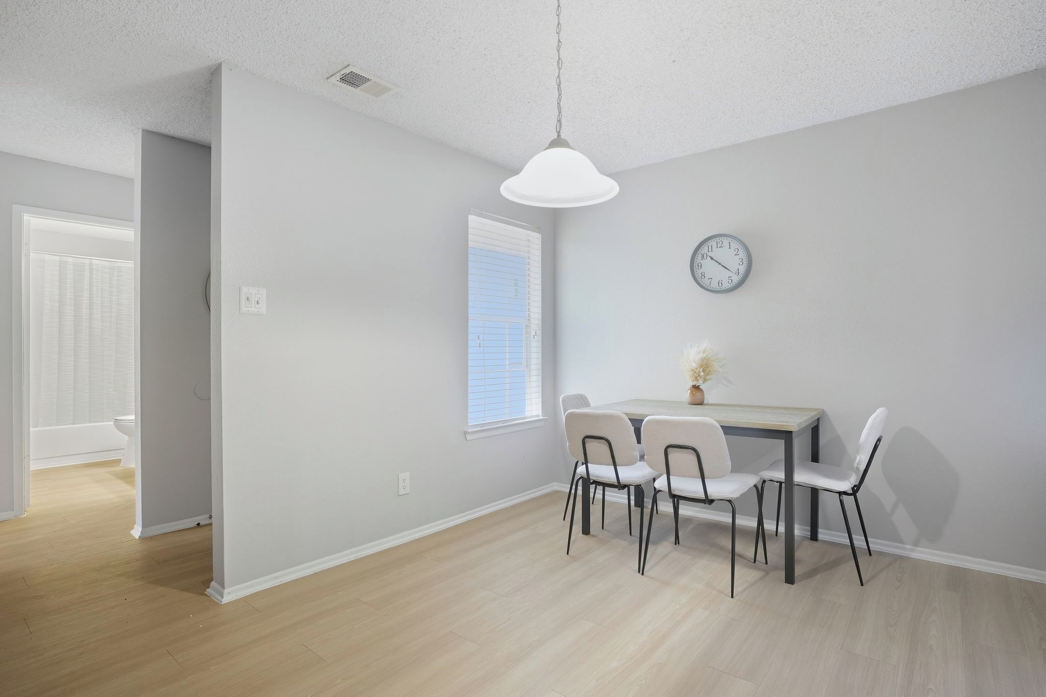 A modern dining area with a table and chairs, a clock on the wall, and a window with blinds.