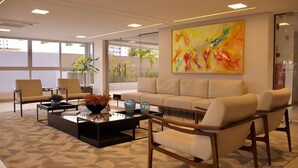 A modern lounge area with a sofa, armchairs, and a coffee table. There is a large abstract painting on the wall and a window providing natural light. - Puerto Ventura #305 - Joao Pessoa by Carpediem (João Pessoa)