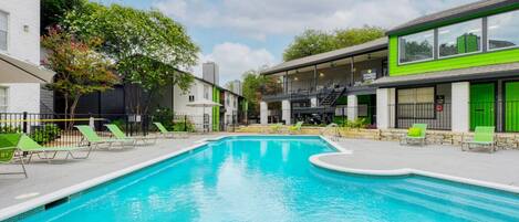 A swimming pool with lounge chairs and a building with a green facade.