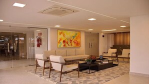A modern waiting area with a sofa, chairs, a coffee table, and a colorful abstract painting. - Puerto Ventura #303 - Flat by the sea in Carpediem (João Pessoa)