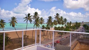A balcony with a view of a beach, palm trees, and a road with cars. - Puerto Ventura #303 - Flat by the sea in Carpediem (João Pessoa)