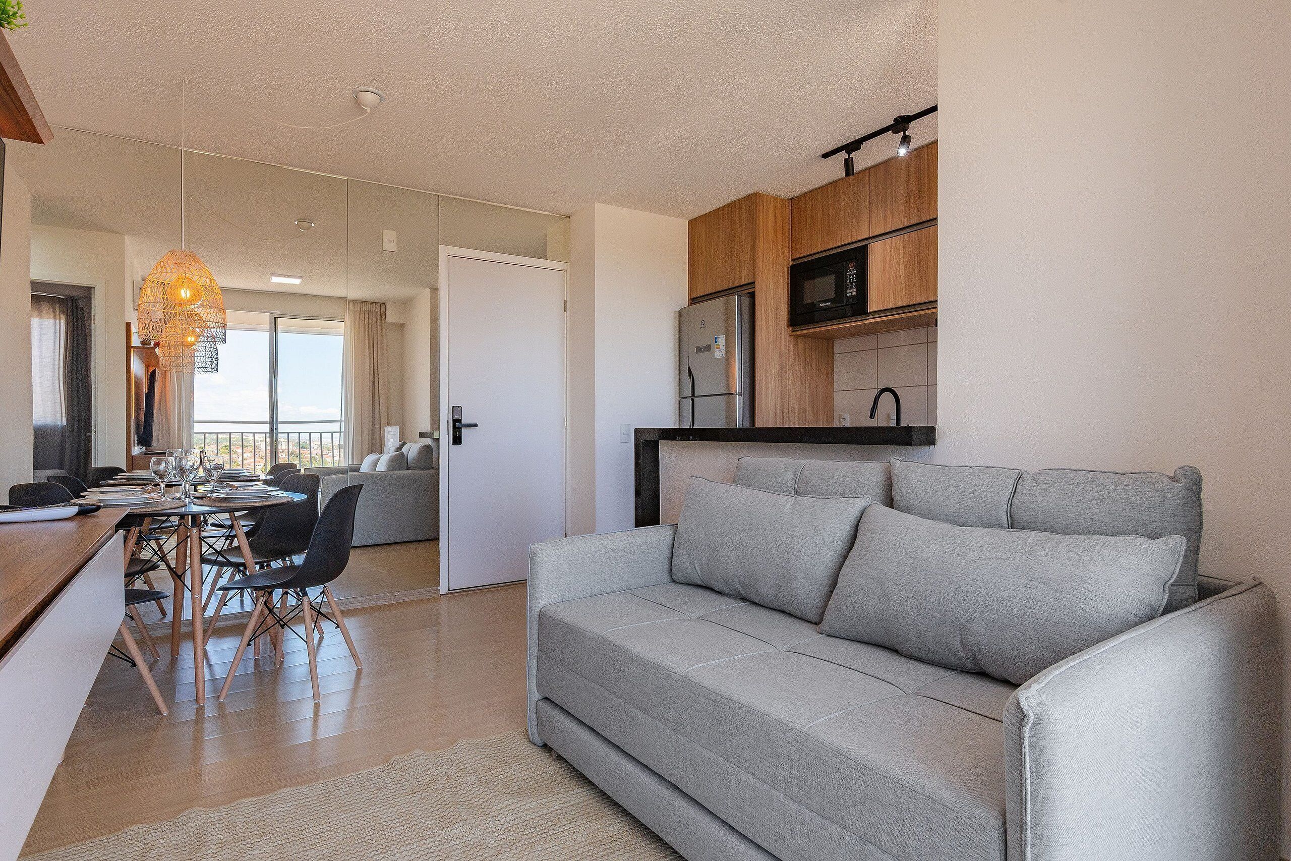 A modern living room with a grey sofa, wooden dining table, and chairs.