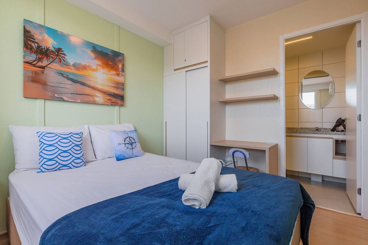Habitación de hotel con cama, un cuadro de un atardecer, baño con espejo y escritorio.