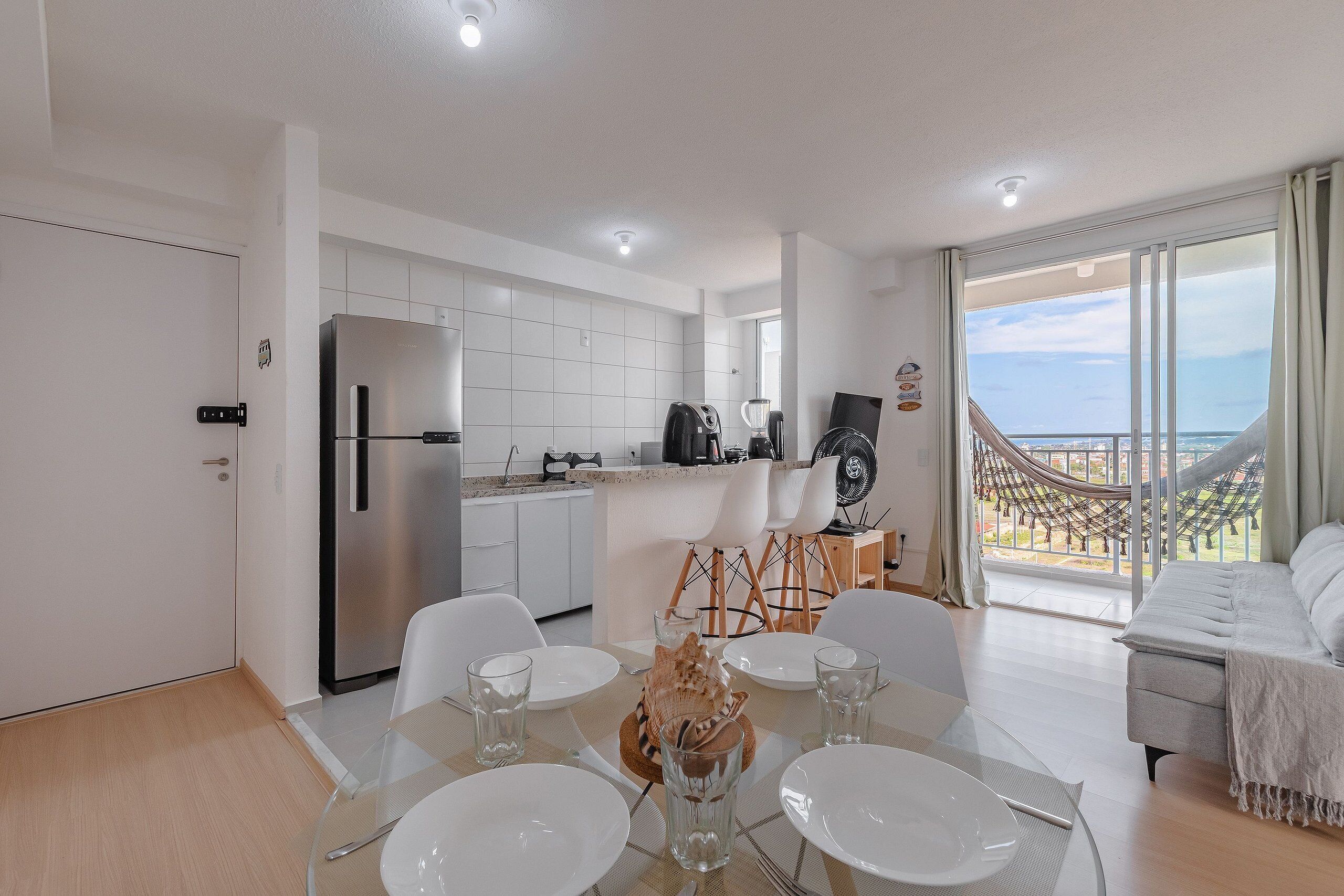 Una cocina moderna con armarios blancos, un refrigerador de acero inoxidable y un comedor con mesa de vidrio y sillas blancas.