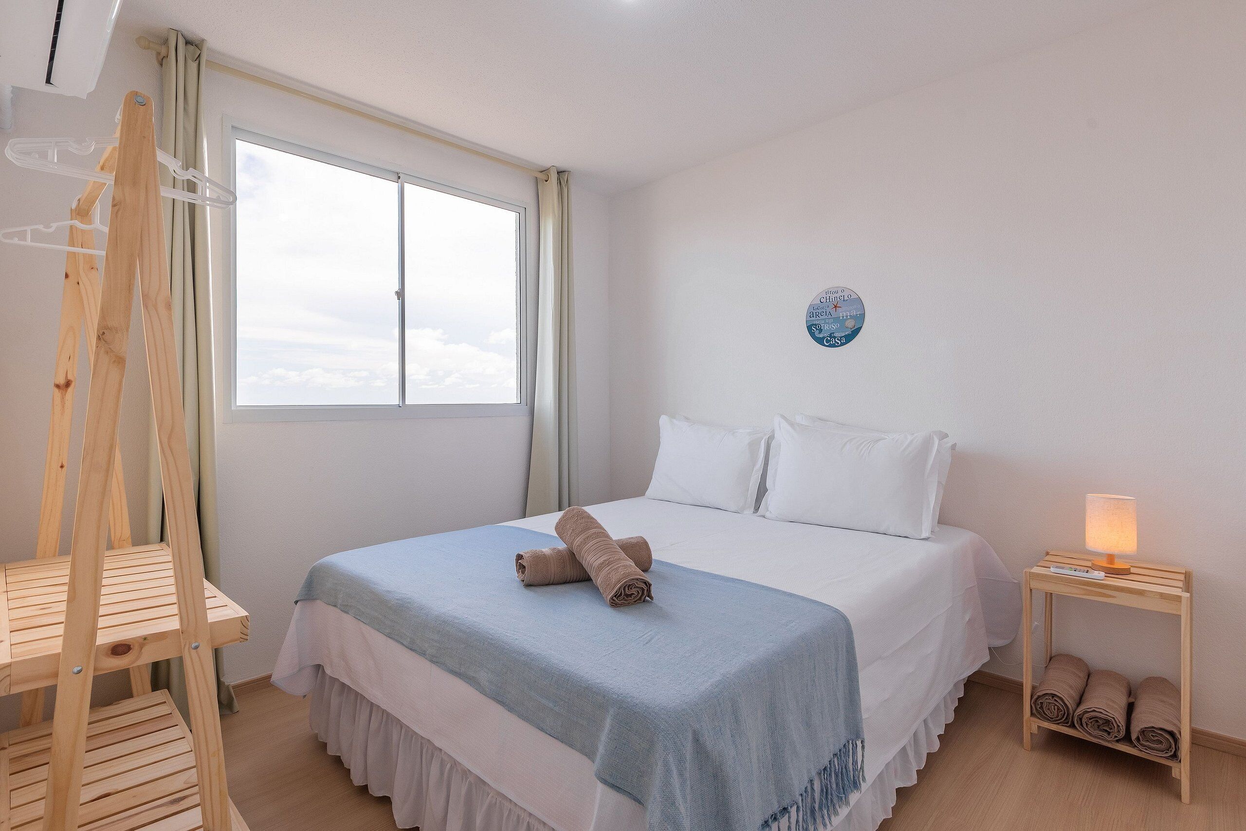 Un dormitorio con una cama, una silla de madera, una mesita de noche con lámpara y una ventana con cortinas.