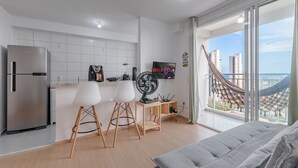 Eine moderne Küche mit einem Kühlschrank, zwei weißen Stühlen, einem Ventilator und einem kleinen Tisch.