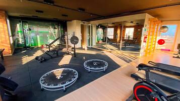 Un gimnasio con equipo de ejercicio, incluyendo cintas de correr y una bicicleta estática, además de un muro con espejos.