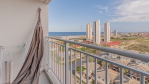 Ein Balkon mit einer Hängematte, mit Blick auf eine Küstenstadt mit Hochhäusern und einem Strand.