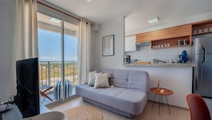 A modern living room with a grey sofa, a small round table, a television, and a balcony with a view. - Mirante #1204 - Apt With Balcony by Carpediem (Fortaleza)