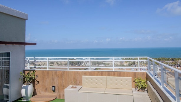 A balcony with a view of the ocean, a wooden bench, and a white planter. - Mirante #1204 - Apt With Balcony by Carpediem (Fortaleza)
