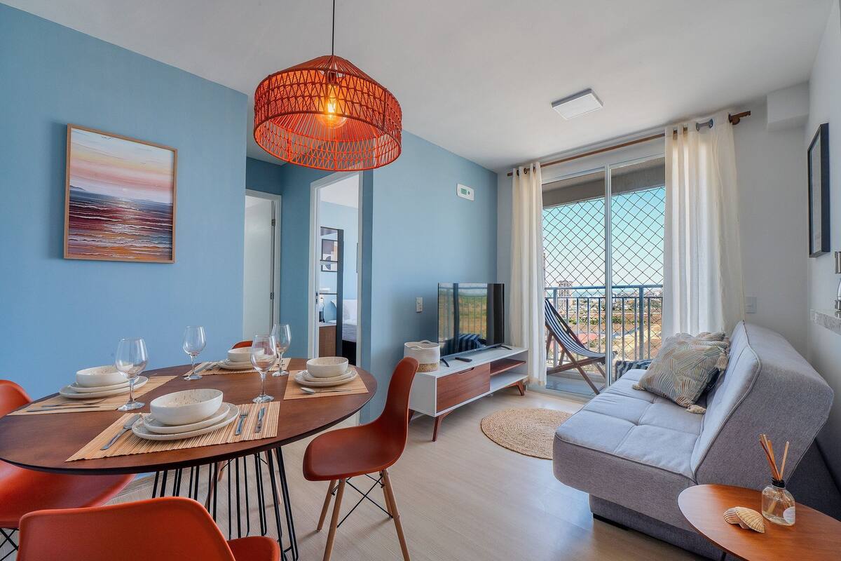 A modern living room with a dining area, a sofa, a TV, and a balcony with a view.