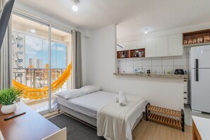 Ein kleines Hotelzimmer mit Bett, Schreibtisch, Pflanze und Blick auf die Stadt durch ein großes Fenster.