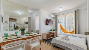 Une chambre d’hôtel moderne comprenant un lit, un coin repas avec une table et des chaises, un téléviseur fixé au mur et un balcon avec vue.