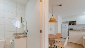 A modern kitchen with white cabinets, a microwave, a refrigerator, and a dining area with a wooden table and chairs. - Mirante #401 - Comfortable Apartment by Carpediem (Fortaleza)