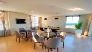 A modern dining area with a round table, grey chairs, a flat-screen TV mounted on the wall, and a large window offering a view of the outdoors. - Mirante #401 - Comfortable Apartment by Carpediem (Fortaleza)
