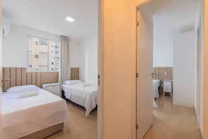 A hotel room with two beds, a window, a bedside table, and a wardrobe. - Mirante #401 - Comfortable Apartment by Carpediem (Fortaleza)