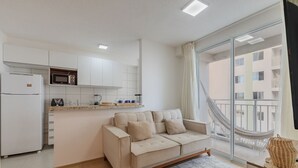 A modern kitchen with white cabinets, a beige sofa, and a large window offering a view of a balcony. - Mirante #401 - Comfortable Apartment by Carpediem (Fortaleza)