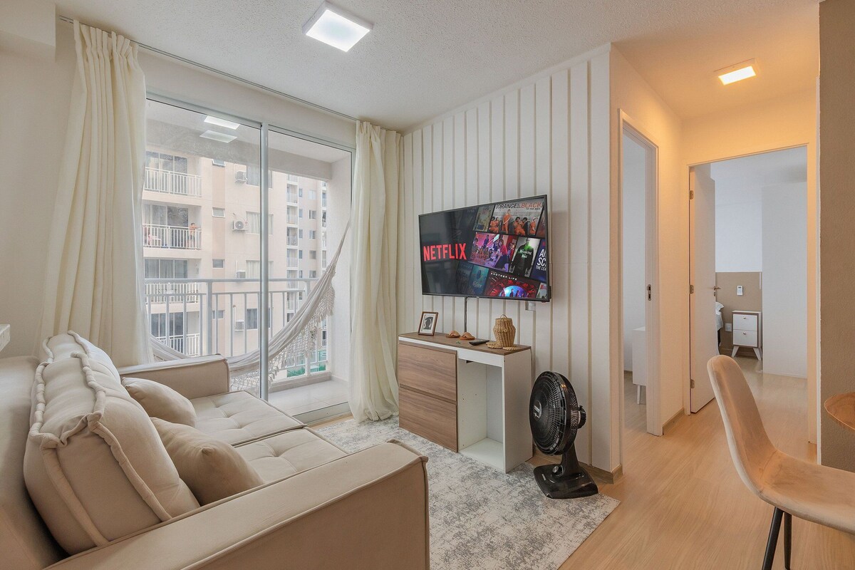 Ein modernes Wohnzimmer mit einer Couch, einem an der Wand montierten Fernseher, einem Schreibtisch und einem Ventilator.