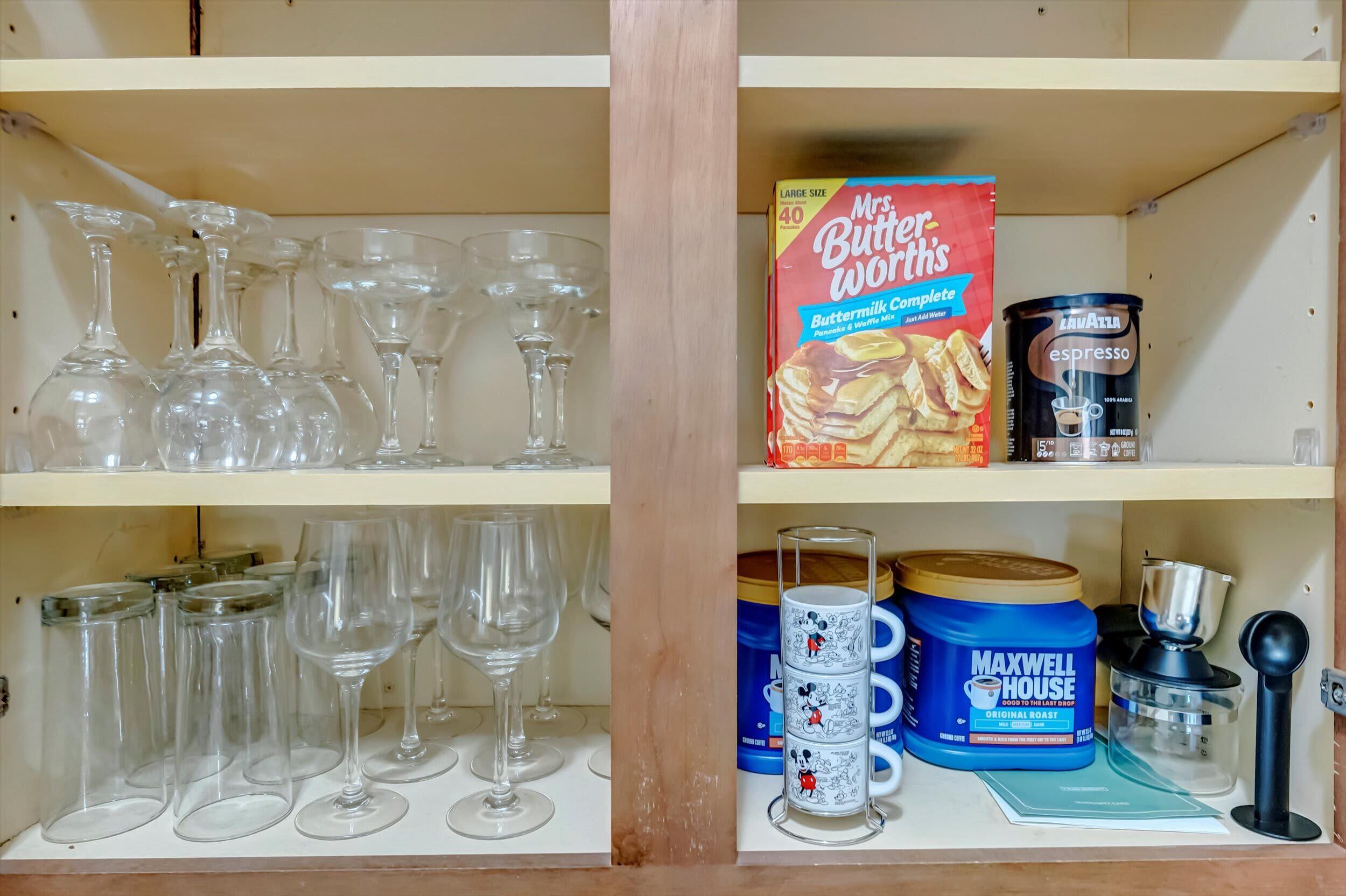 A kitchen shelf with various items including a box of Mrs. Butterworth's Buttermilk Complete, a can of Lawatta espresso, and Maxwell House coffee.