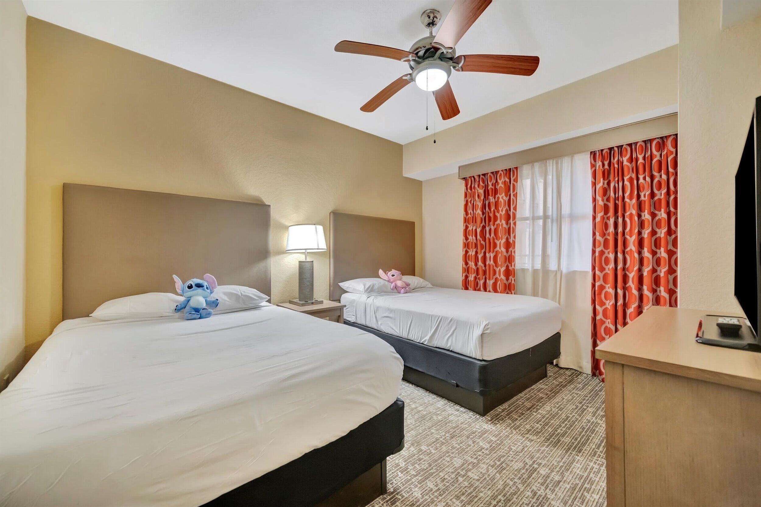 Une chambre d’hôtel avec deux lits, un ventilateur de plafond, un bureau et un téléviseur.