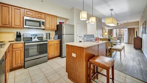 A modern kitchen with wooden cabinets, stainless steel appliances, and a central island with stools. - Top Floor 3B Balcony 10 Mins to Disney NO Fees (Orlando)
