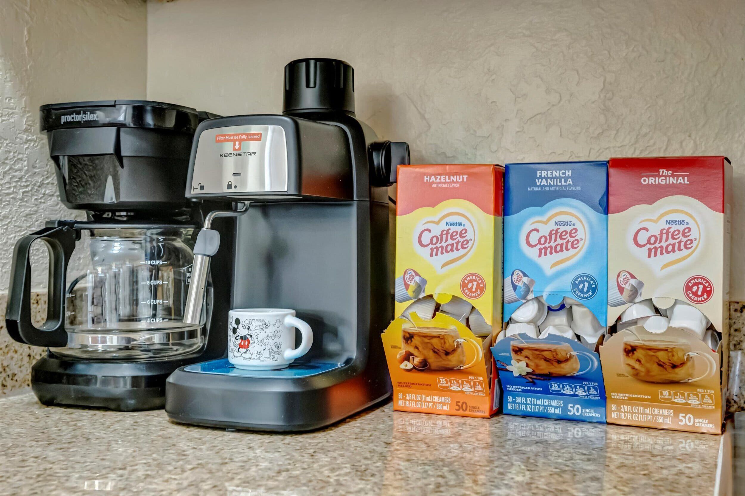 A Keurig coffee maker, a mug, and three boxes of Nestlé Coffee Mate creamer.