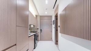 A narrow hallway with light wood cabinetry, a built-in oven, and a washing machine. - Stayshort - Amazing Studio in JVC That Sleeps 2 With Balcony (Dubai)