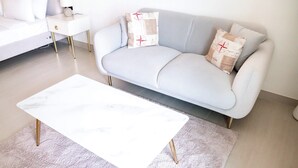 A modern living room with a light blue sofa, a white coffee table, and a small white side table with a lamp. - Stayshort - Amazing Studio in JVC That Sleeps 2 With Balcony (Dubai)