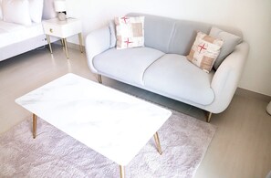 A modern living room with a light blue sofa, a white coffee table, and a small white side table with a lamp. - Stayshort - Amazing Studio in JVC That Sleeps 2 With Balcony (Dubai)